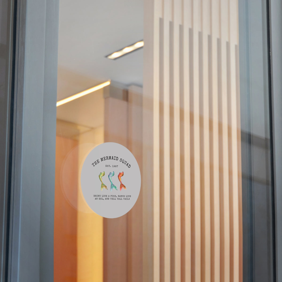 The Mermaid Squad round vinyl sticker in grey, shown on a glass door