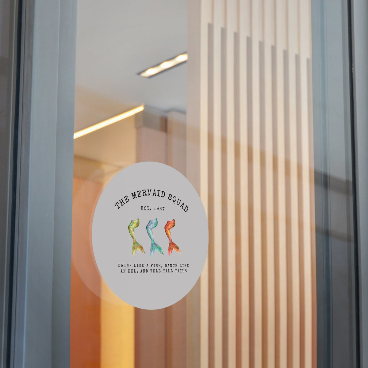 The Mermaid Squad round vinyl sticker in grey, shown on a glass door, alternate view
