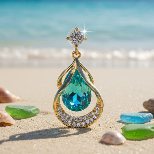 Teardrop-shaped gemstone earring on a sandy beach with shells and seaglass.